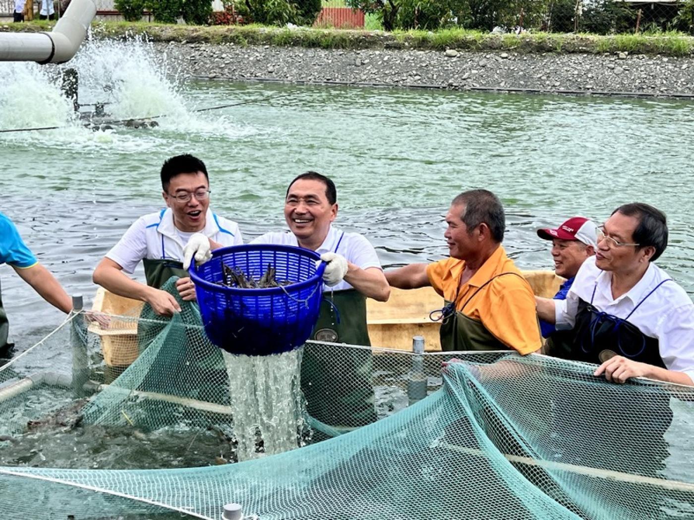 國民黨總統參選人侯友宜（左2）參訪屏東縣鹽埔鄉泰國蝦養殖專區，現場換上青蛙裝，走入水深及大腿的養殖池中與漁民一起體驗撈蝦。 中央社