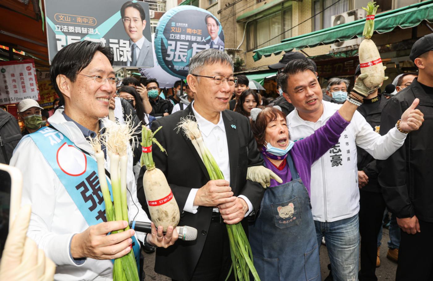 柯文哲（前左2）2日陪同張其祿（前左）前往木新市場掃街拜票，有攤商送上蘿蔔與蒜苗並高聲祝賀「凍蒜」。中央社